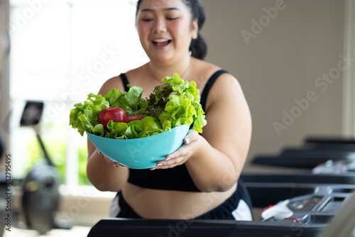 Obraz na płótnie Portrait fat woman enjoying eating vegetable salad. beautiful young chubby overweight woman wearing sporty fitness clothes doing exercise indoors at gym fitness sport club, body and health care w salonie