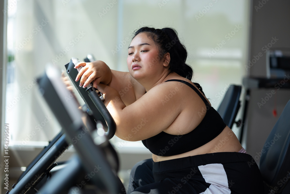 Tired fat asian woman on cycling. beautiful young chubby overweight woman wearing sporty fitness clothes doing exercise indoors at gym fitness sport club, body and health care