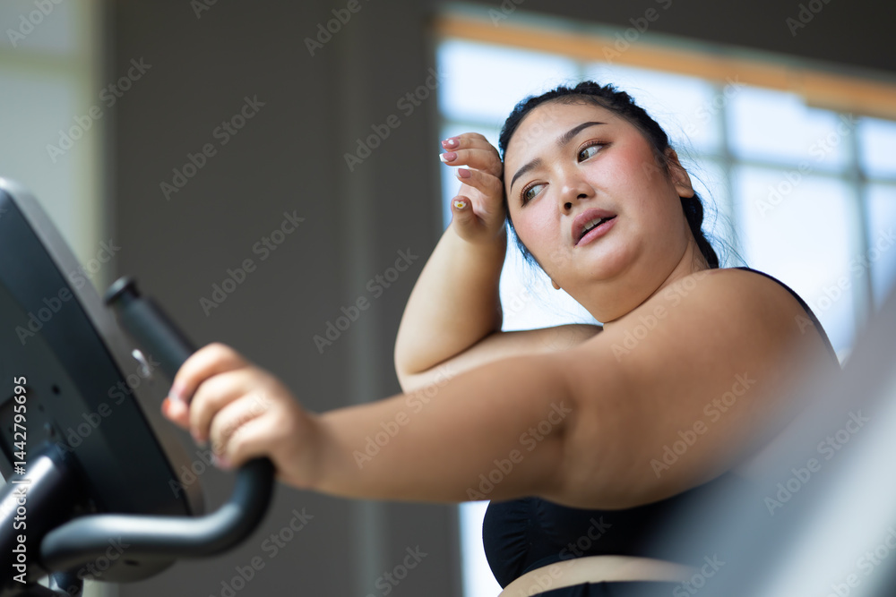 Tired fat asian woman on cycling. beautiful young chubby overweight woman wearing sporty fitness clothes doing exercise indoors at gym fitness sport club, body and health care