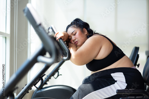 Obraz na płótnie Tired fat asian woman on cycling. beautiful young chubby overweight woman wearing sporty fitness clothes doing exercise indoors at gym fitness sport club, body and health care w salonie