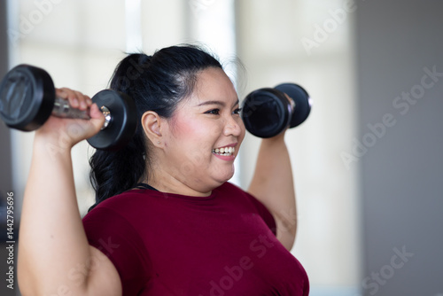 Obraz na płótnie Young woman exercising with dumbbells. beautiful young chubby overweight woman wearing sporty fitness clothes doing exercise indoors at gym fitness sport club, body and health care w salonie