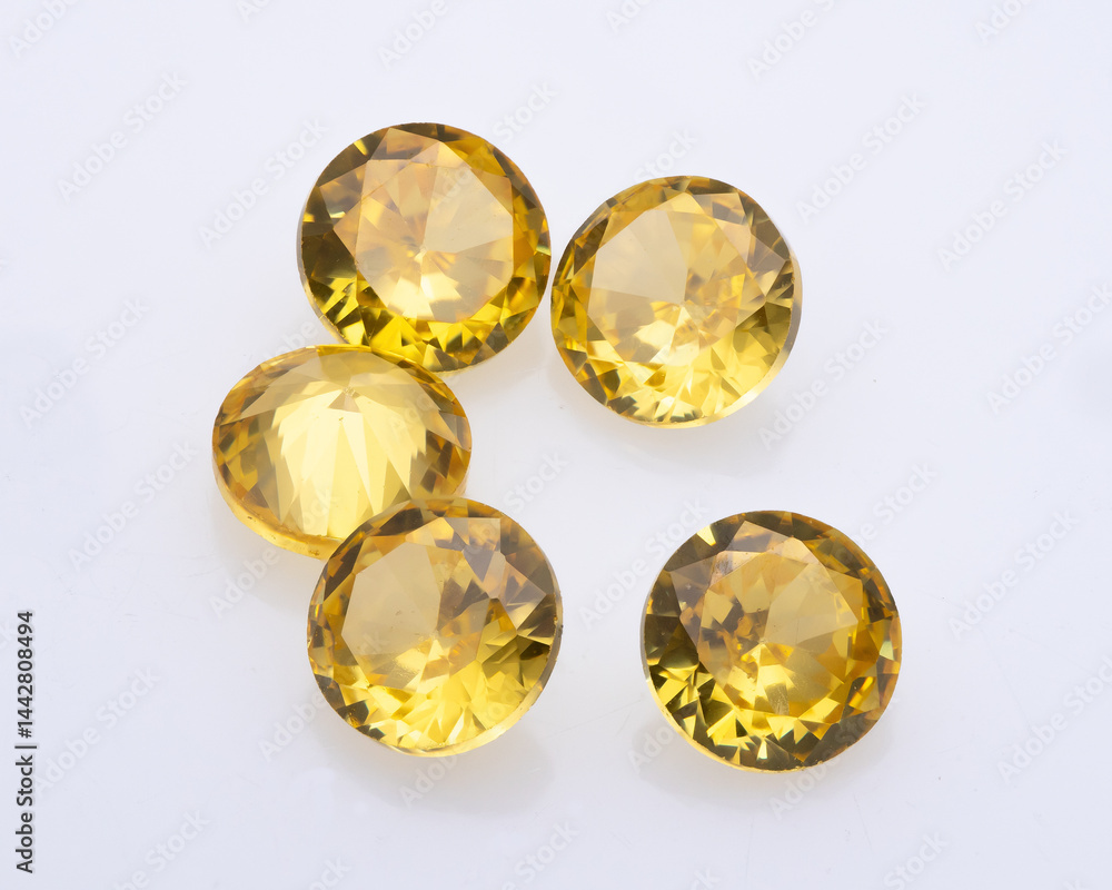 Five round cut citrine gemstones are arranged on a white surface, showcasing their faceted brilliance and warm yellow hue in studio lighting