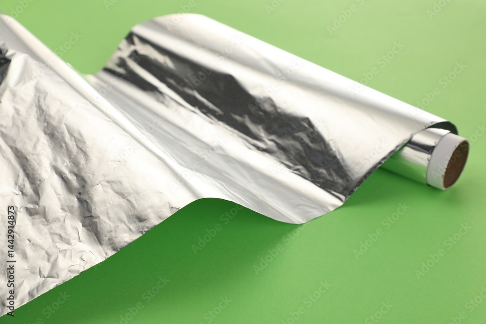Roll of aluminum foil on green background, closeup
