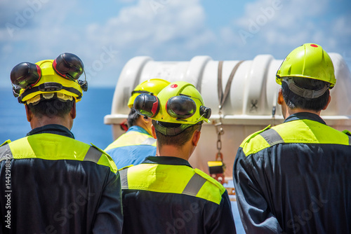 Fotografie A group of sailors standing by the lifeboats, listening attentively to the deck officer’s instructions on how to use the lifeboats and evacuate the ship, emphasizing safety training and preparedness