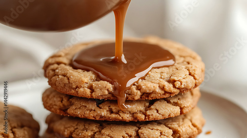 Caramel sauce being poured over stack of three crumbly cookies, creating rich and indulgent dessert scene with warm tones and soft background