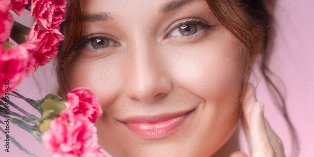 Close-up of a smiling young Caucasian woman with pink carnations on soft pastel background. Ideal for beauty, skincare, floral fragrance, wellness, and feminine lifestyle promotions.