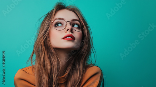Beautiful young woman looks up with curiosity on teal background 