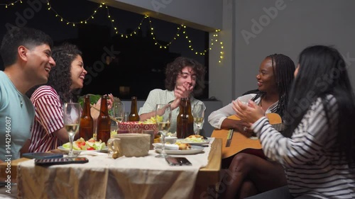 young black woman plays guitar at an evening gathering while her Latin friends clap and dance