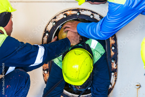 Fototapeta Naklejka Na Ścianę i Meble -  Crew member wearing breathing apparatus exits a narrow hatch after providing first aid during a man evacuation drill from a confined space on a merchant ship.