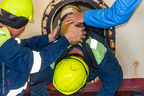 Картината върху платно Crew member wearing breathing apparatus exits a narrow hatch after providing first aid during a man evacuation drill from a confined space on a merchant ship