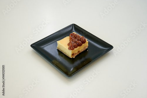 Obraz na płótnie A slice of cheesecake with nuts on top. It is on a black plate. The plate is on a white table w salonie