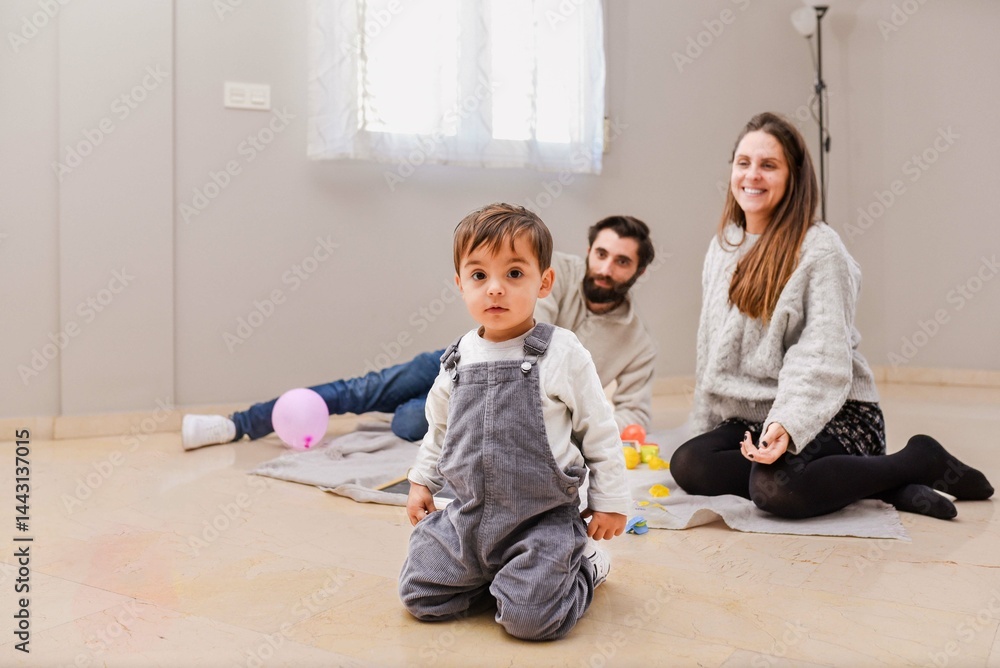 Naklejka premium Happy family sitting on the floor and playing with their toddler son at home