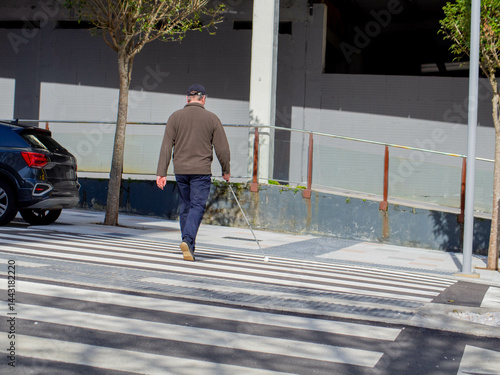 A sightless man walking on the crosswalk using his guide cane
