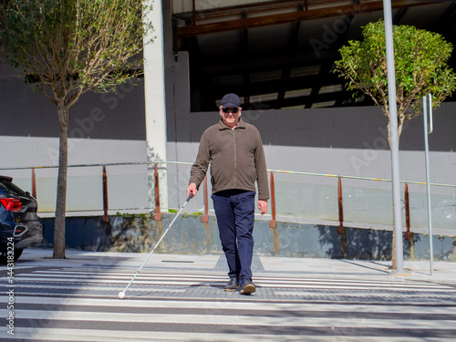 A blind man crossing the street with his white cane, moving forward cautiously.