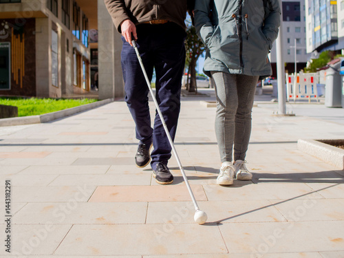Vászonkép Front view of a sightless man walking on the pavement using his cane and a woman providing guidance
