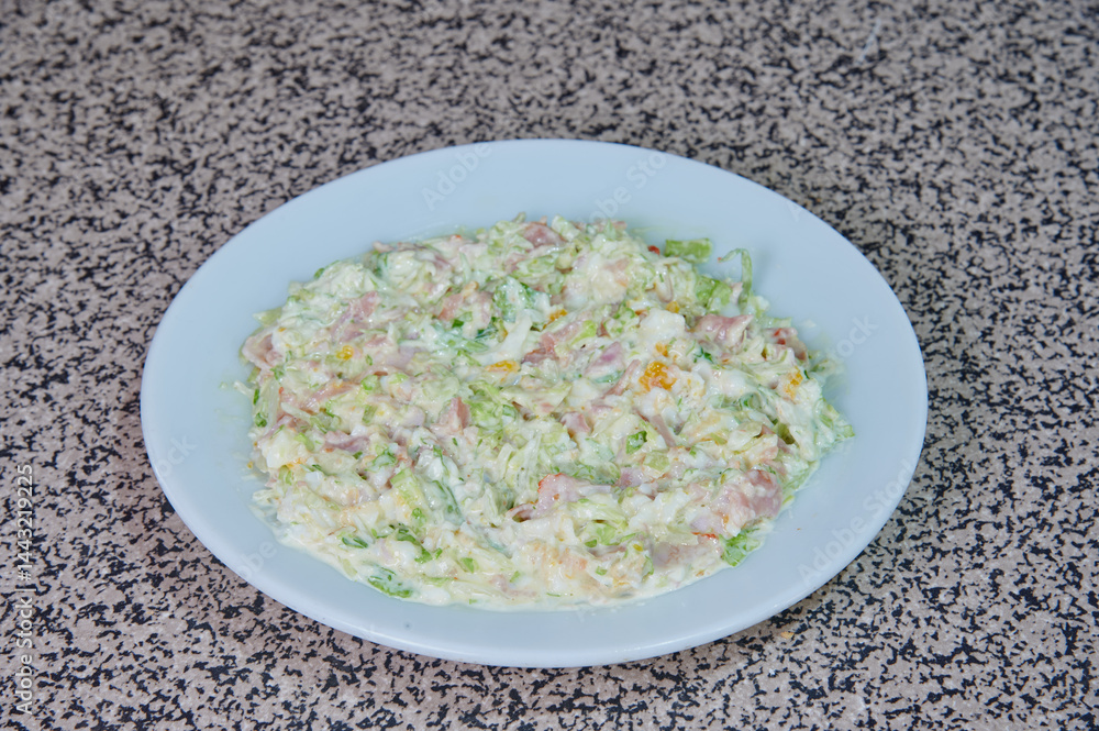 A white plate with a salad on it. The salad is made of lettuce, cheese, and ham