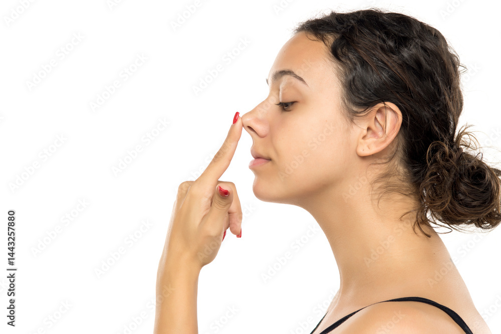 Profile view of young woman gently touching nose with closed eyes. Gentle gesture suggesting rhinoplasty consideration. Studio portrait on white background Profile view of young woman gently touching nose with closed eyes. Gentle gesture suggesting rhinoplasty consideration. Studio portrait on white background