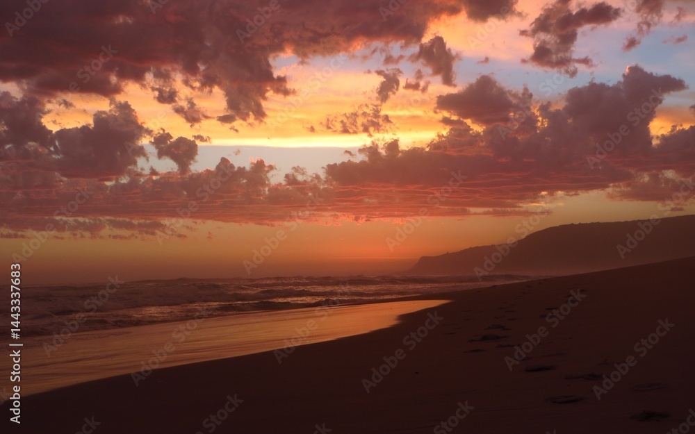 Fototapeta premium A tranquil beach scene at sunset with vibrant clouds reflecting warm hues, serene waters, and a peaceful atmosphere in Nature's valley, South Africa