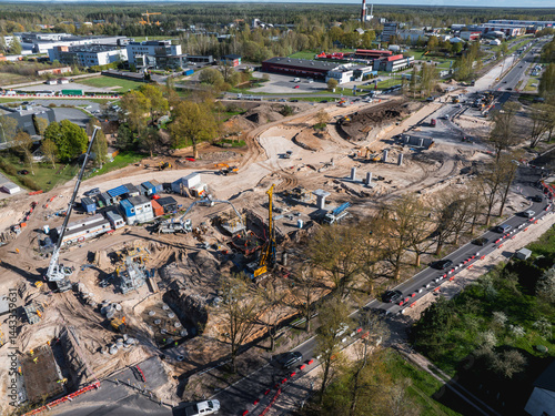 Obraz na płótnie Active construction site with cranes, drilling equipment, and materials. Urban and green areas surround the site, with roads and vehicles nearby. w salonie