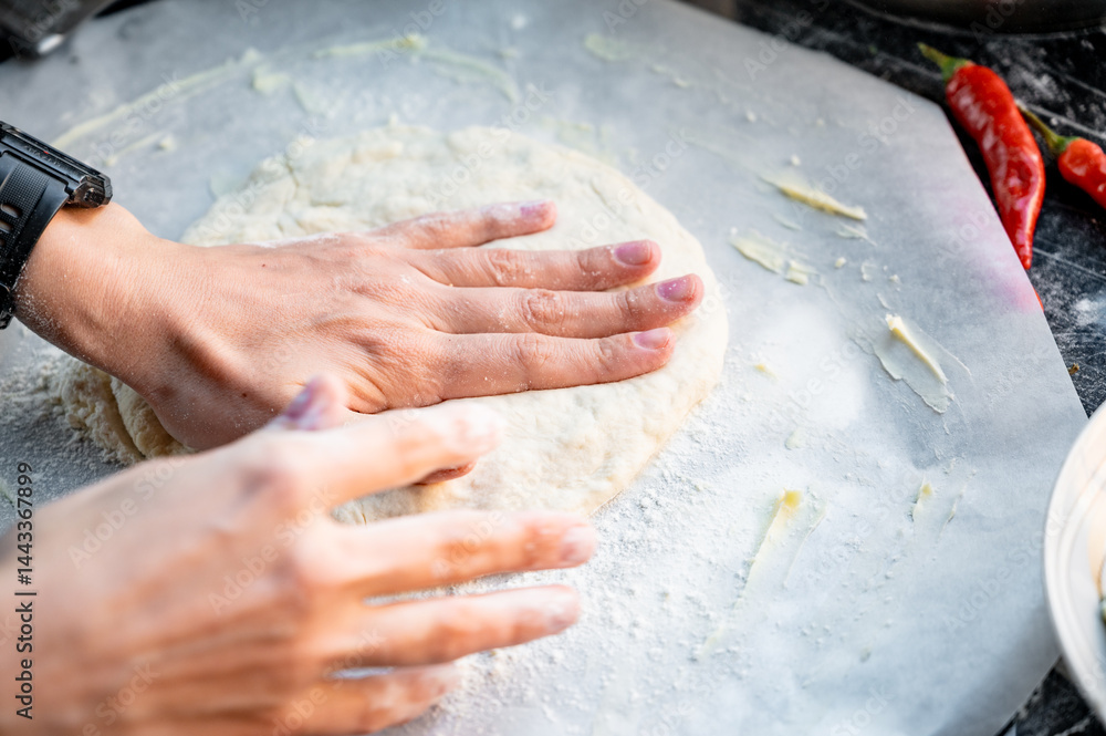Making homemade pizza with three types of cheese - women's hands in action. Close-up scene of women's hands rolling out homemade pizza dough on a kitchen countertop.