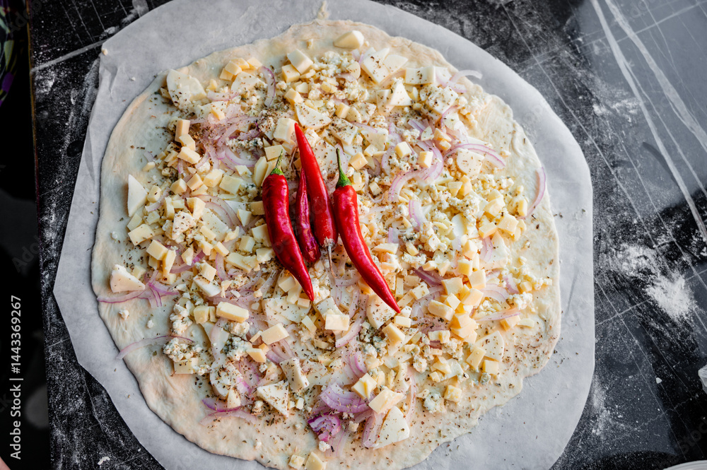 A homemade pizza in its raw form, assembled with toppings. The dough is uncooked but fully prepared with sauce, cheese, and fresh ingredients. The kitchen is cozy and softly lit, with utensils, bowls,