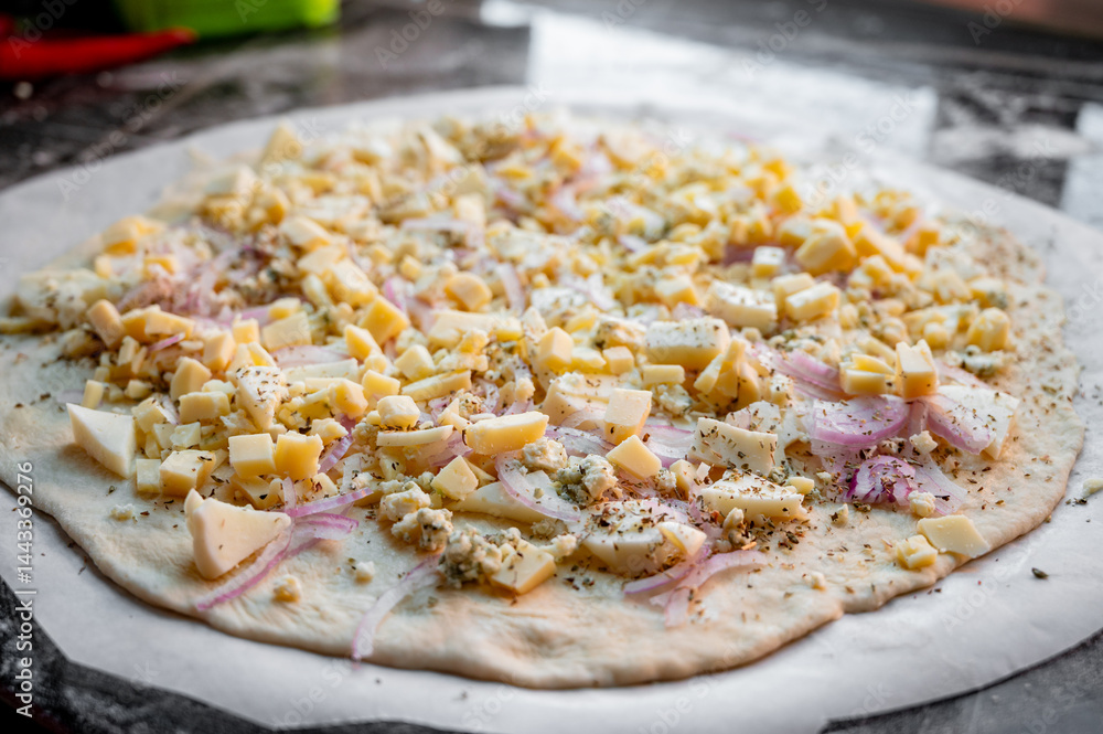 A homemade pizza in its raw form, assembled with toppings. The dough is uncooked but fully prepared with sauce, cheese, and fresh ingredients. The kitchen is cozy and softly lit, with utensils, bowls,