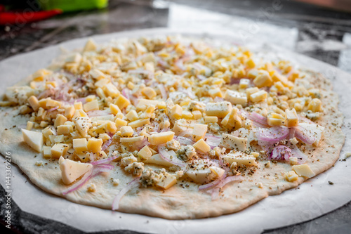 Obraz na płótnie A homemade pizza in its raw form, assembled with toppings. The dough is uncooked but fully prepared with sauce, cheese, and fresh ingredients. The kitchen is cozy and softly lit, with utensils, bowls, w salonie