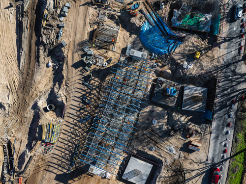 Obraz na płótnie Aerial view of a construction site in Riga, Latvia, featuring a steel framework, workers, machinery, dirt roads, and visible progress on infrastructure. w salonie