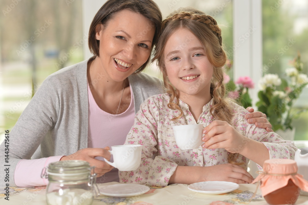 Happy mom and daughter drinking tea at home