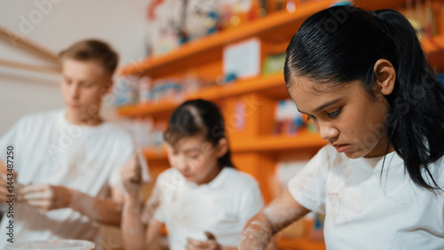 Smart teenager modeling cup of clay while laughing at art lesson. Diverse happy student standing while doing creative activity at workshop. Creative activity concept. Blurred background. Edification.