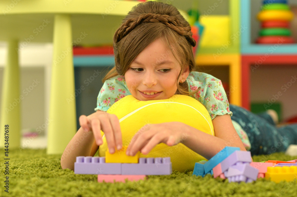 Portrait of cute girl playing with colorful plastic blocks in room