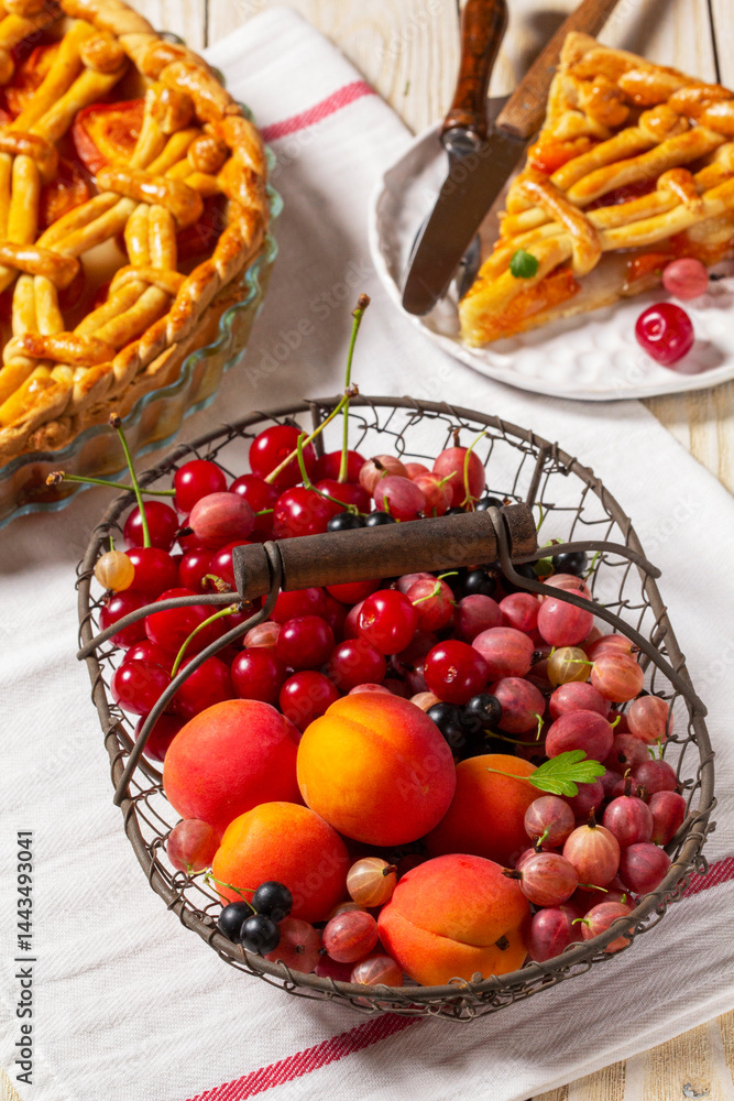 Metal basket with fruits and berries and apricot pie, decorated with pastry ornament.