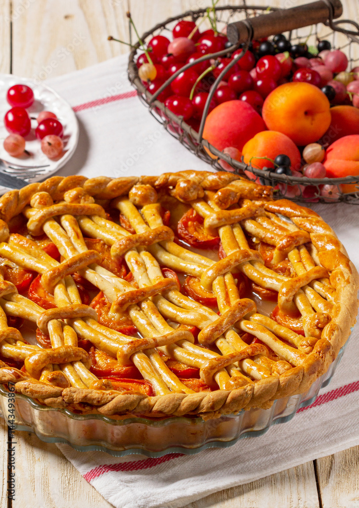 Apricot pie decorated with dough ornament and a metal basket with fruits and berries.