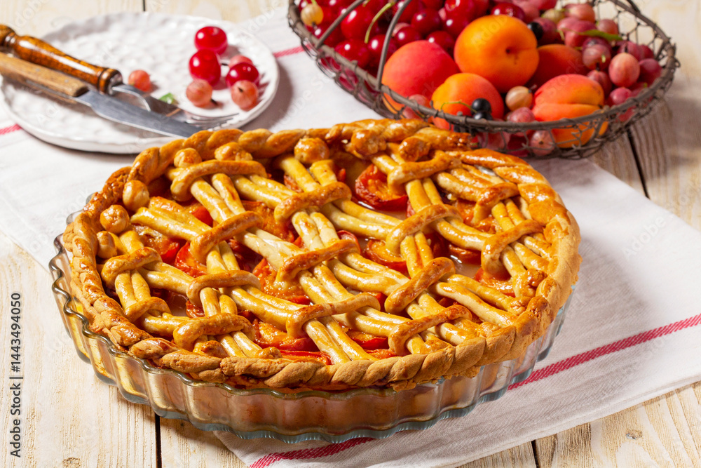 Apricot pie decorated with dough ornament and a metal basket with fruits and berries.