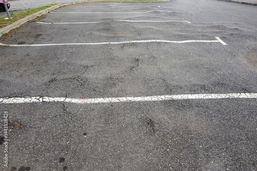 An empty parking lot features multiple cracked asphalt surfaces by trees roots