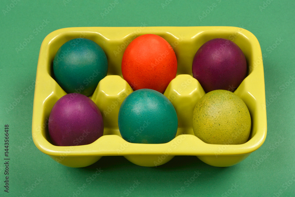 A slightly angled top-down shot shows a light green ceramic egg carton with six colorful Easter eggs on a solid green background