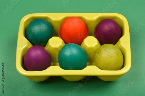 Obraz na płótnie A slightly angled top-down shot shows a light green ceramic egg carton with six colorful Easter eggs on a solid green background w salonie