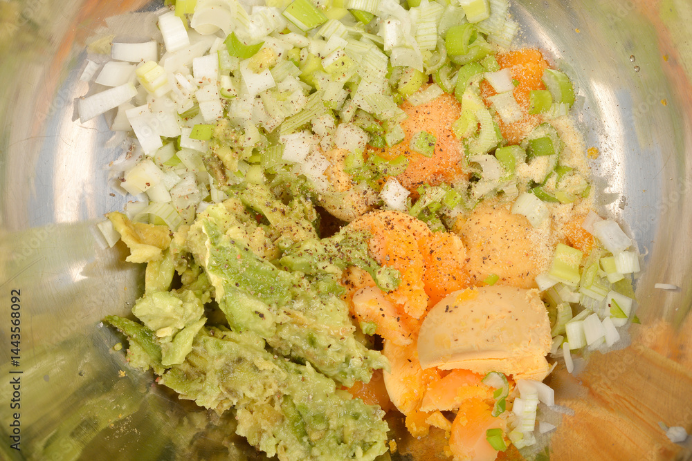 A close-up top-down view shows ingredients in a stainless steel bowl: mashed avocado, chopped onions, spices, and yolks, being mixed for deviled egg filling
