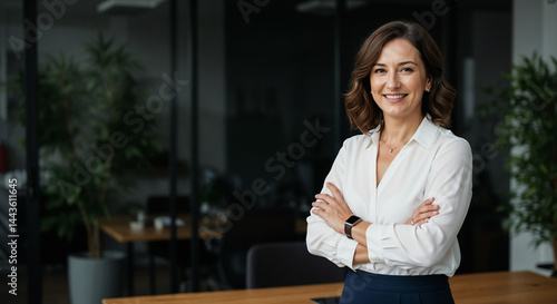 A business woman is standing with her arms crossed in a professional office environment.

