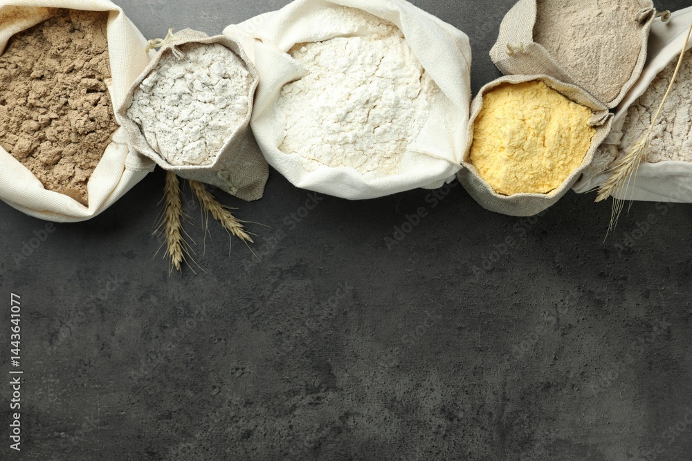Different types of flour in bags on grey table, flat lay. Space for text