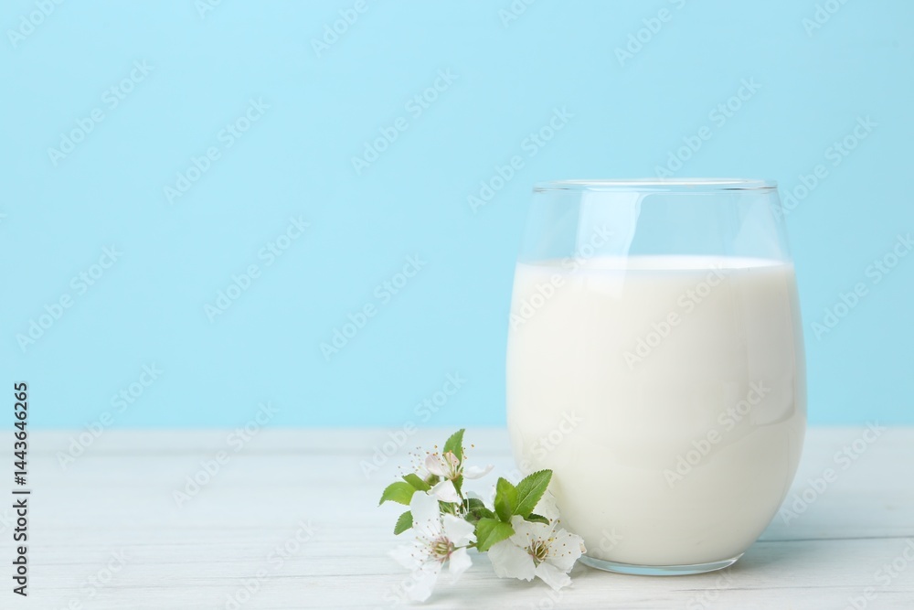 Glass of fresh milk and blossoms on white wooden table against light blue background. Space for text Glass of fresh milk and blossoms on white wooden table against light blue background. Space for text