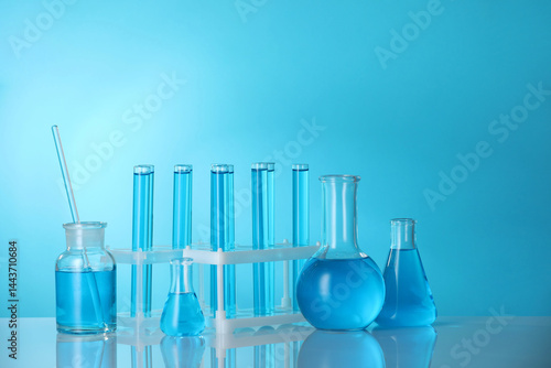 Laboratory glassware with liquid on mirror surface against blue background. Space for text