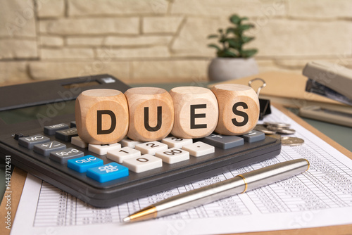 Dues text on wooden blocks with calculator and financial documents in office background.