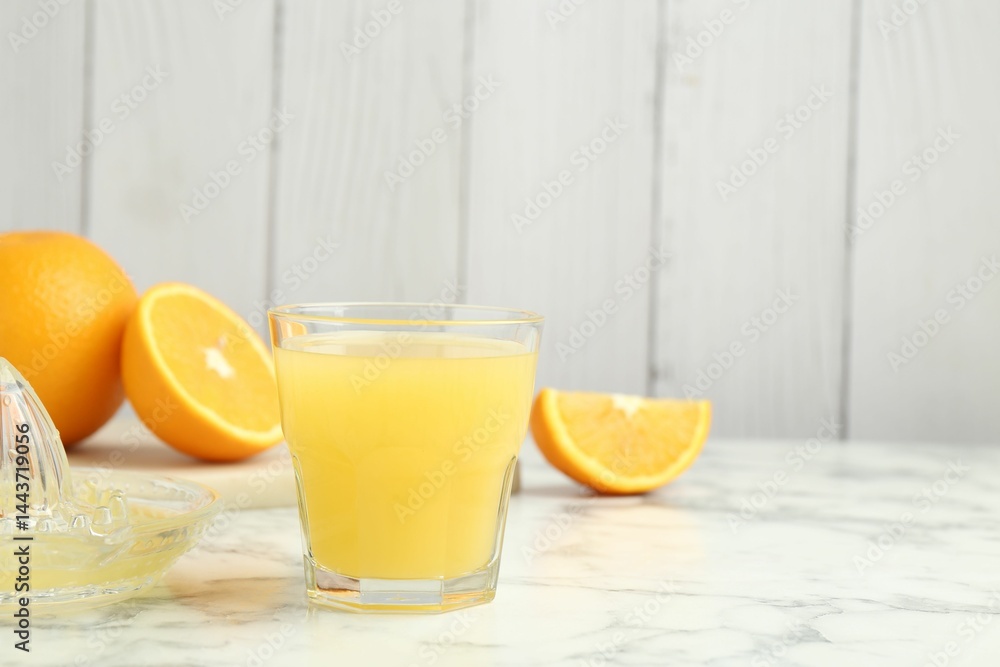 Fototapeta premium Fresh orange juice, fruits and squeezer on white marble table against wooden background, closeup. Space for text