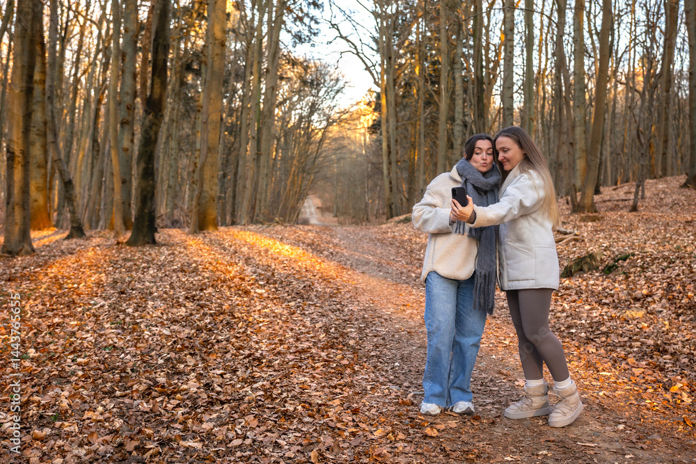 Fototapeta premium Two friends taking a selfie on their phone in the forest. Friends in nature.