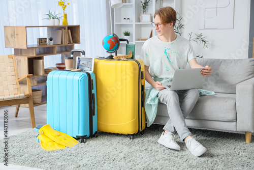 Male tourist with laptop and suitcases booking hotel room online at home