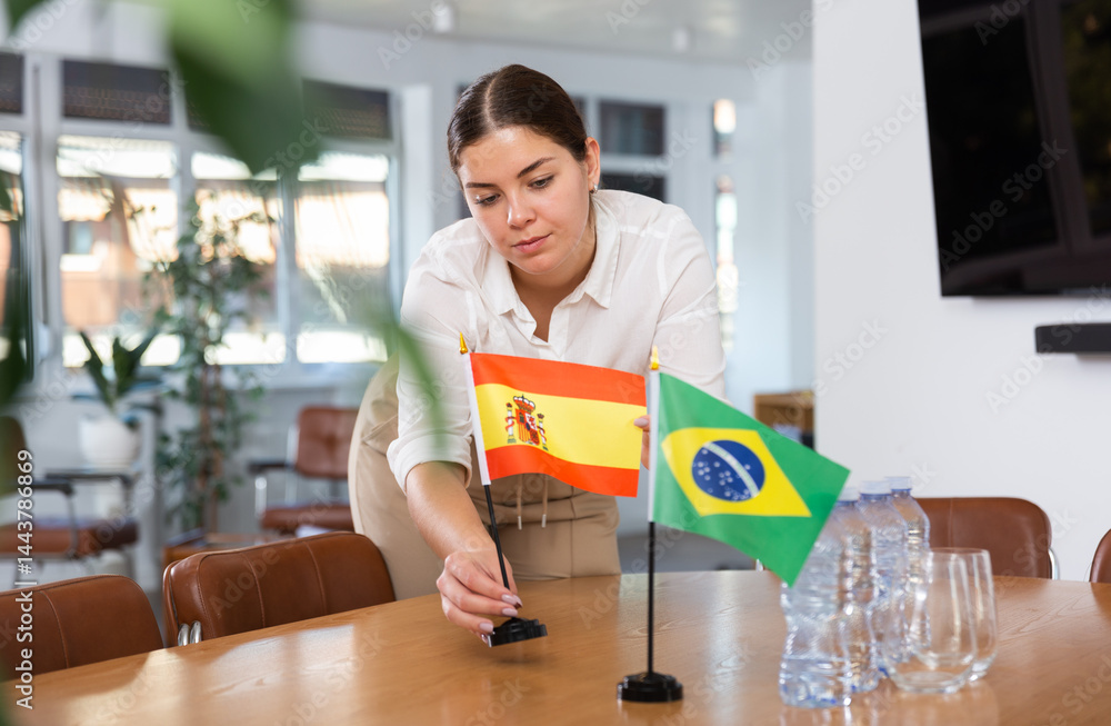 Young female assistant setting up flags of brazil and spain on table for international negotiations Young female assistant setting up flags of brazil and spain on table for international negotiations