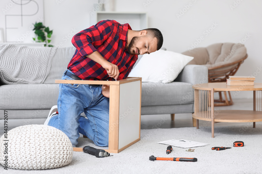 Young man with drill assembling table at home