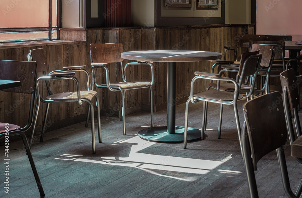 Table at a restaurant with sunlight coming in through the Large windows, casting beautiful light and shadow patterns on the dining table and chairs at empty restaurant. use it as your Wallpaper,Poster