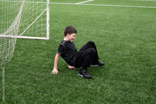 Young boy smiling while sitting on soccer field astro turf
